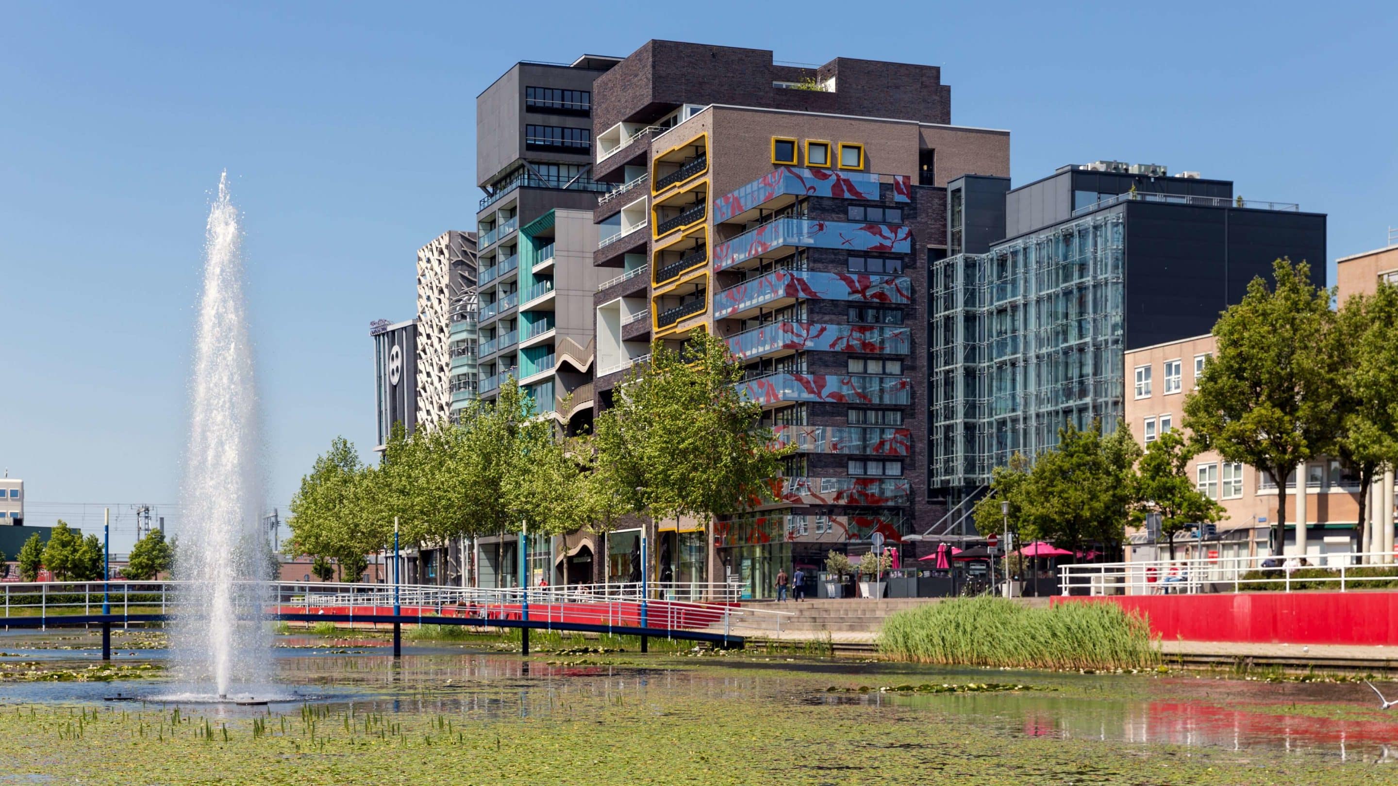 Een vijver met een brug en kantoorpanden op de achtergrond.